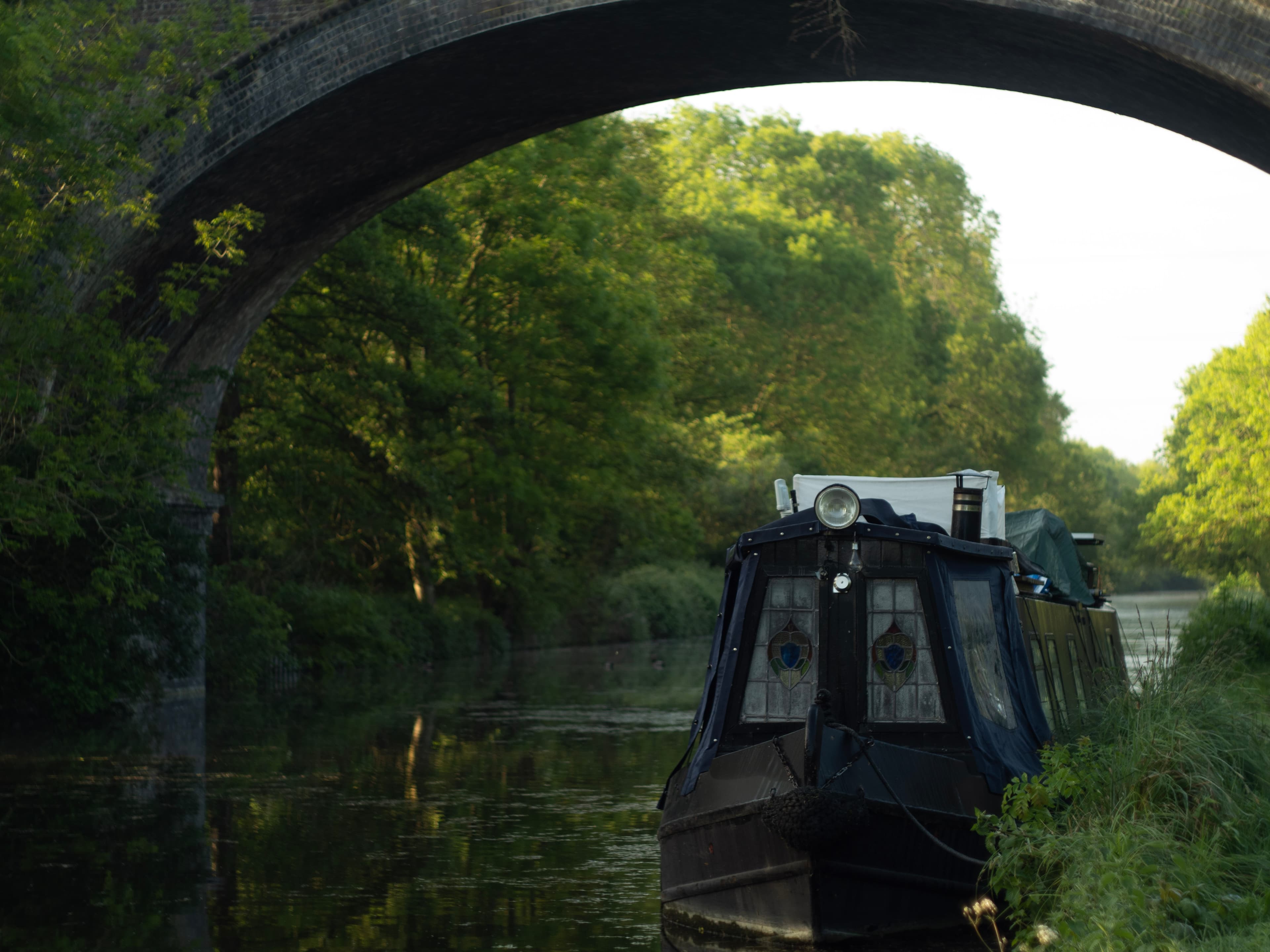 A narrowboat moored under a stone bridge on the canal at golden hour
